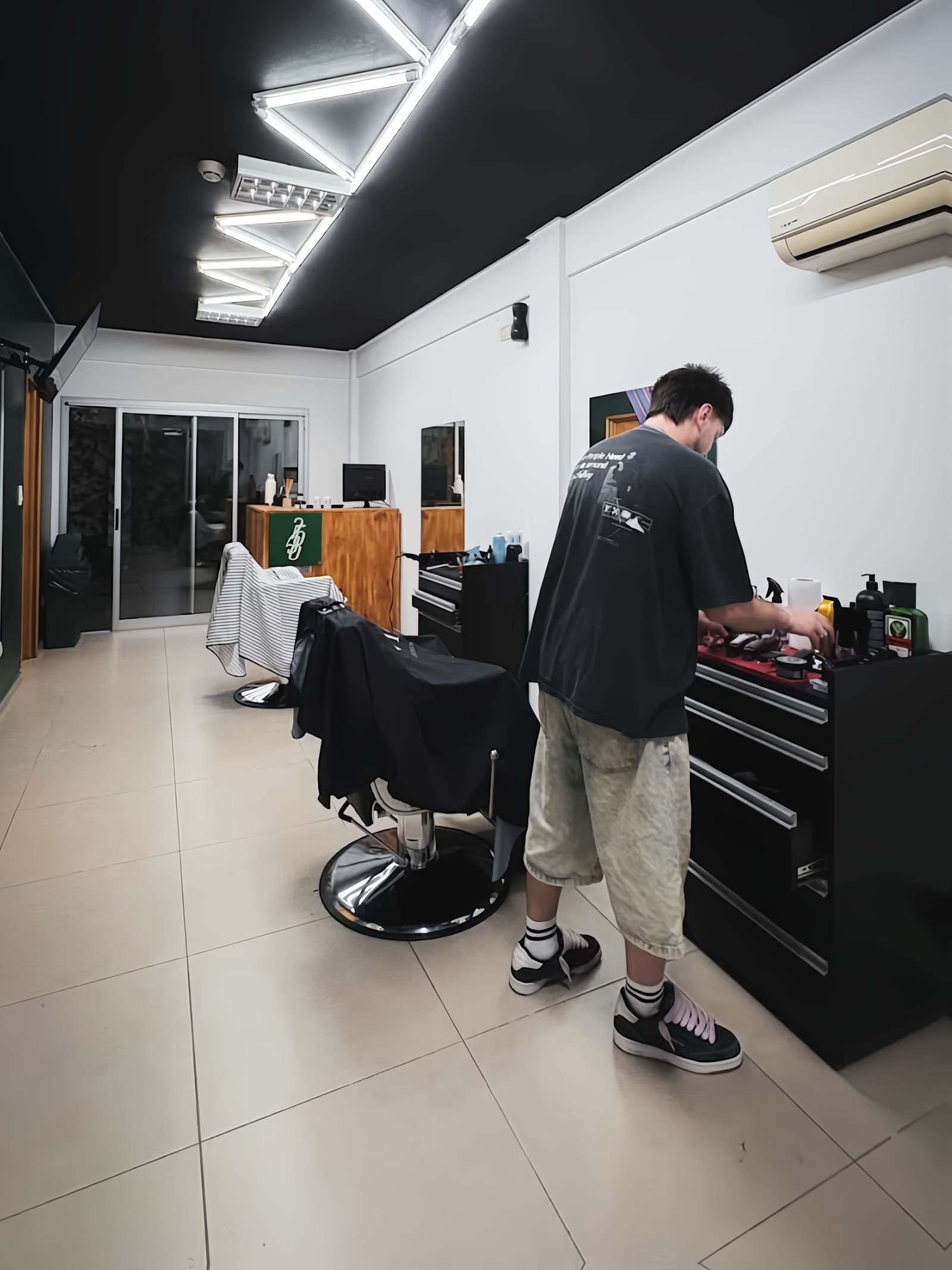 Interior de Veinticinco Ocho: dos sillones de barbero, la estación de trabajo y los tubos de luz en zigzag del techo